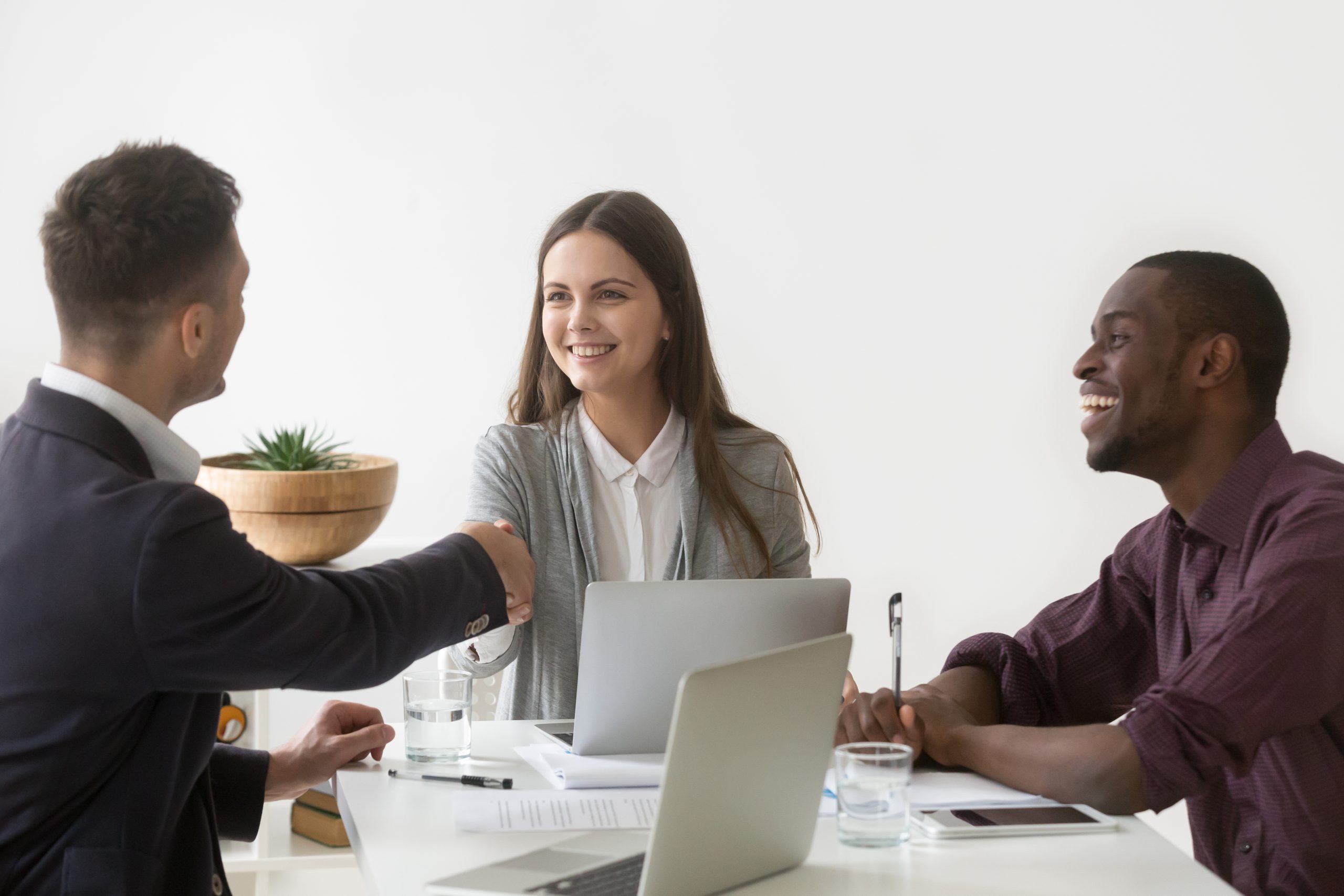 Smiling businesswoman shaking hand of male partner at group meet Smiling millennial businesswoman shaking hand of male partner at diverse group negotiation, friendly woman boss handshaking new team member at meeting, showing respect or making contract deal concept