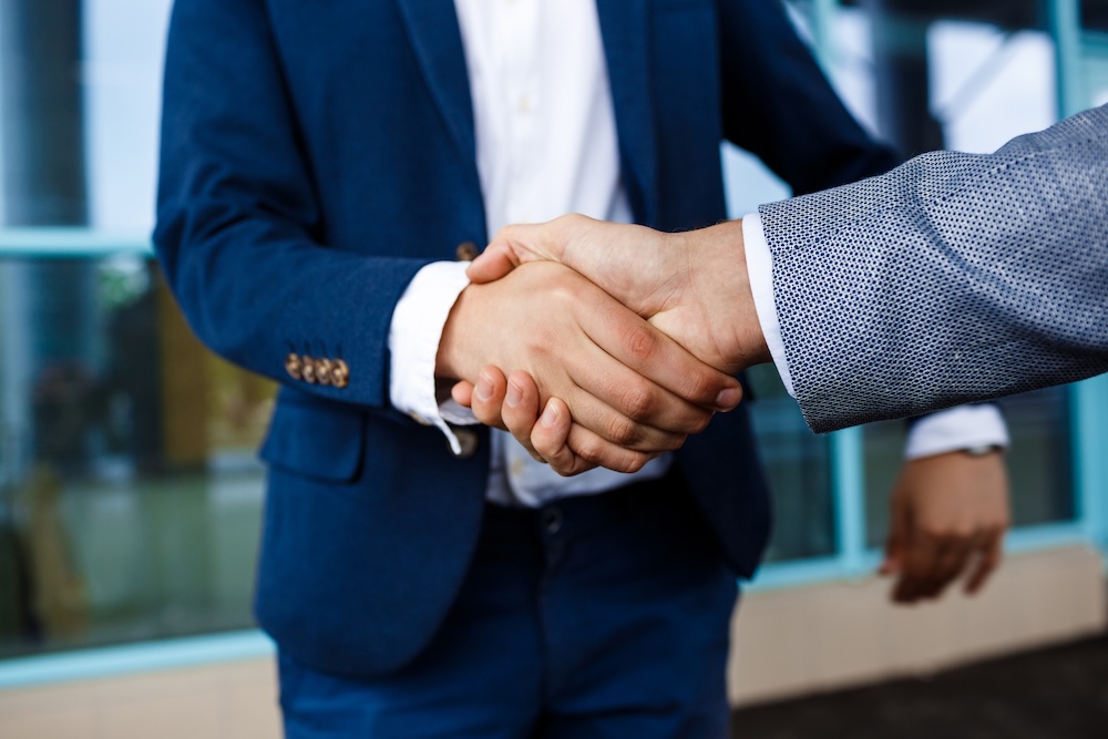 Picture of two young businessmen on street background shake hands